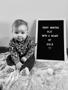 a baby sitting next to a sign that says eight months old with a heart of gold