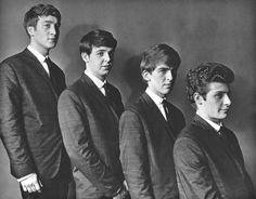 four young men in suits and ties posing for the camera, with one looking at the camera