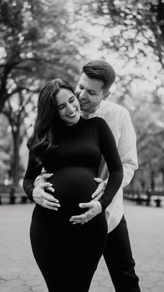 a pregnant couple cuddles in the park for their black and white photo session