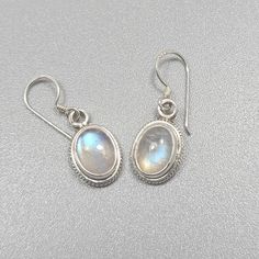 Sterling silver earrings with blue moonstone settings. Classical style, gemstones have a pretty blue reflection. Dimensions with hook: 25mm x 9mm, or 0.98 inch x 0.35 inch. Dimensions pattern: 11mm x 9mm, or 0.43 inch x 0.35 inch.  Gemstone 8mm x 6mm, or 0.31 inch x 0.24 inch. Weight silver and gemstone: 2.8gm/0.10oz Hypoallergenic Silver Moonstone Jewelry, Sterling Silver Oval Cabochon Earrings, Silver Nickel-free Moonstone Earrings, White Oval Moonstone Earrings, Silver Oval Cabochon Earrings, Silver Moonstone Gemstone Earrings, Silver Moonstone Earrings With Ear Wire, Round Moonstone Cabochon Earrings, Silver Cabochon Dangle Earrings