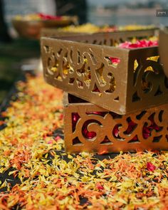 two decorative boxes sitting on top of colorful shredded paper and plastic flowers in the background