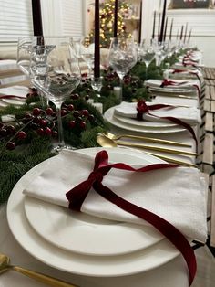 the table is set with white plates, silverware and red ribbon on them for christmas dinner