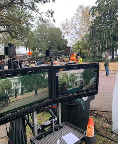 two monitors are set up on the side of a road with people in the background