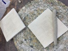 three pieces of white tile sitting on top of a rock next to a plastic bag