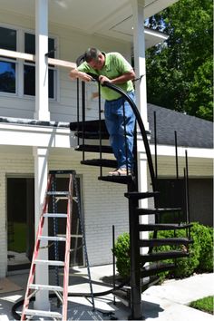 a man standing on top of a stair case next to a white house with trees in the background