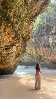 a woman standing in front of a large rock formation on top of a sandy beach