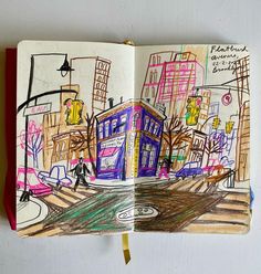 an open book with colored drawings on the pages and in front of a cityscape