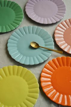 four different colored paper plates with a gold spoon in the middle one has a fork on it