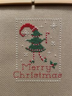 a cross stitch christmas card with a tree on it and the words merry christmas written in red