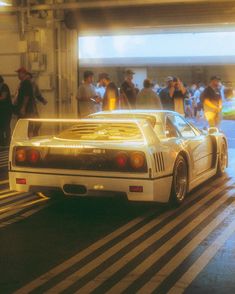 a white sports car driving down a street next to a group of people in the background