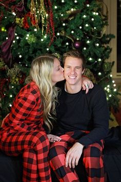 a man and woman sitting in front of a christmas tree with their arms around each other