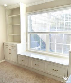 an empty room with built in bookshelves and drawers on either side of the window