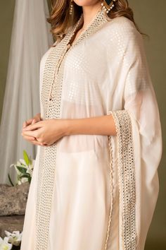 Ivory cape with mirror embroidered borders. Comes with embroidered blouse and sharara.
Component: 3
Pattern: Embroidery
Type Of Work: Mirror work
Neckline: Cape: Open
Sleeve Type: Blouse: Half, Cape: Three quarter
Fabric: Organza, Silk
Color: Ivory
Other Details: 
Attached lining
Approx weight (in kgs): 3
Closure: Sharara: Button
Occasion: Destination Wedding - Aza Fashions Blouse And Sharara, Half Cape, Organza Cape, Embroidery Mirror Work, Embroidery Mirror, Organza Embroidery, Open Sleeve, Sharara Set, Pattern Embroidery