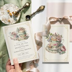 a hand holding a wedding card next to a plate with a tea cup on it