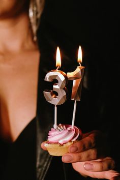 a woman is holding a cupcake with candles in the shape of number thirteen on it