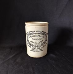 a white ceramic cup with black writing on the bottom and inside, sitting on a black background