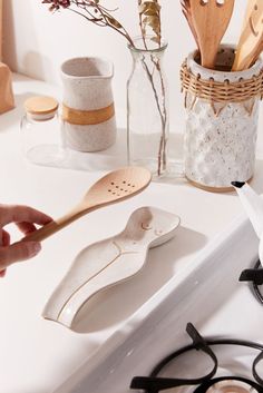 a person is holding a wooden spoon over a stove top with various kitchen utensils