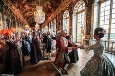 several people dressed in period costumes dance together inside an ornate room with chandeliers