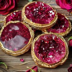 three pieces of red and gold jewelry sitting on top of a wooden table next to roses