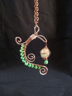 "Copper color wire wrap design featuring green seed beads and a swirling green glass bead \"lantern\" Indulge your whimsical side with this charming and uniquely one of a kind accessory, perfect for adding a bit of playful magic to any outfit! All my pieces are handmade creations. The item pictured is the item that will be shipped to you, though colors may vary slightly from picture due to differences in monitor settings.  Check out my shop for more charms and creative jewelry, or message me if you have a specific idea in mind!" Whimsical Green Nickel-free Jewelry, Green Glass Wire Wrapped Necklaces, Green Glass Wire Wrapped Necklace, Whimsical Green Jewelry For Gifts, Adjustable Whimsical Green Necklace, Green Wire Wrapped Czech Glass Necklace, Wire Wrapped Green Glass Jewelry, Green Wire Wrapped Glass Jewelry, Whimsical Green Necklace