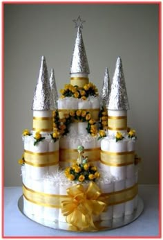 a white cake with yellow flowers and gold ribbons on it's sides, topped with an elaborately decorated castle