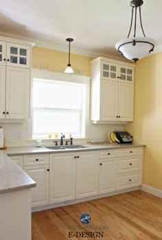 an empty kitchen with white cabinets and wood flooring, along with a light fixture hanging from the ceiling