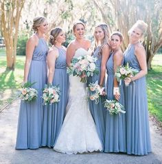 a group of women standing next to each other in front of trees and grass with bouquets