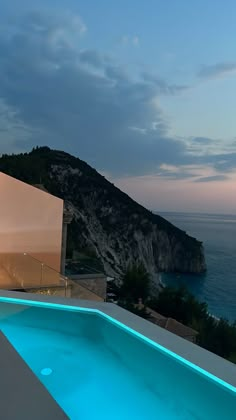 an outdoor swimming pool next to the ocean at night with lights on and water running down it