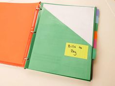 an orange and green binder with bills attached to it next to a notepad