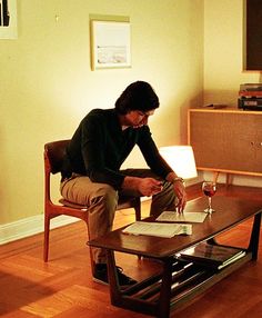 a man sitting in a chair with a glass of wine next to him on the coffee table