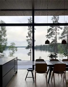 a dining room table with chairs and an island in front of large windows overlooking the water