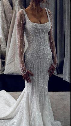 a woman standing in front of a mirror wearing a wedding dress with long sleeves and beading