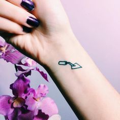 a woman's hand with a small tattoo on her wrist and purple flowers in the background