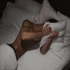 a shirtless man laying in bed with white sheets and pillows on top of him