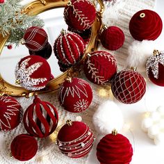 red and white christmas ornaments are on a table next to a mirror with gold trimmings