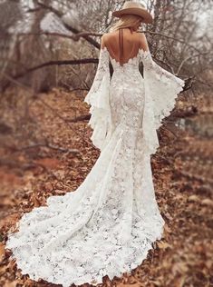 a woman in a white dress and hat standing in leaves with her back to the camera