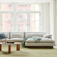 a living room filled with lots of furniture next to large windows on top of a green rug