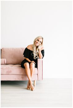 a woman sitting on top of a pink couch with her legs crossed and smiling at the camera