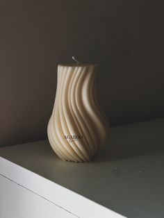 a white vase sitting on top of a table next to a wall with a candle in it