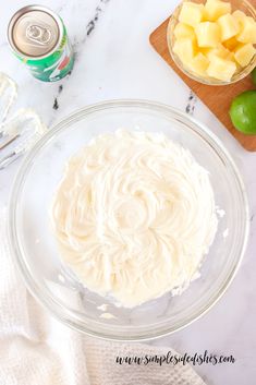 a bowl filled with white frosting next to two cans of soda and limes