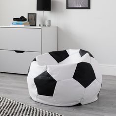 a black and white soccer ball bean bag sits on the floor next to a dresser