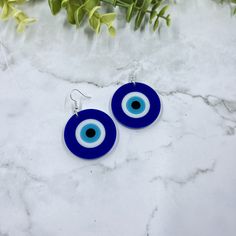 blue and white evil eye glass earrings on marble surface with green plant in the background