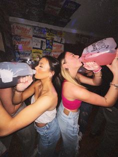 three girls are drinking from plastic bottles in a bar while one girl is holding a bottle