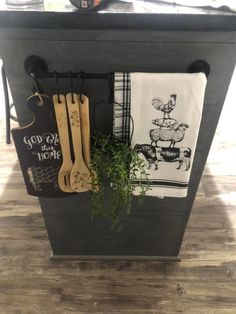 kitchen utensils hanging on the side of a black trash can with herbs in it