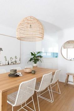 a dining room table with white chairs and rattan lamps hanging from the ceiling over it