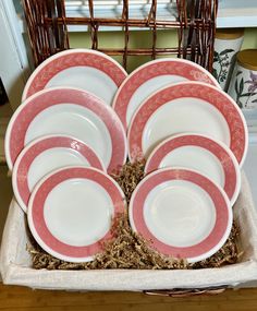 a set of pink and white plates in a basket on top of a wooden table