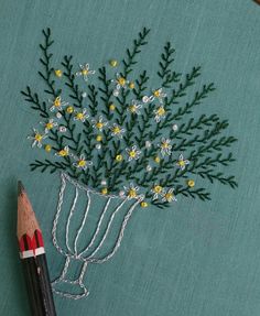 a pencil and some flowers on a piece of cloth with embroidery work in the background