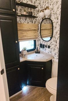 the bathroom is decorated in black and white with floral wallpaper, wood flooring, and a round mirror