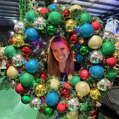 a woman standing in front of a christmas wreath with ornaments on it and smiling at the camera