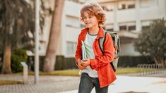 a young boy walking down the street with a book in his hand and a backpack on his back